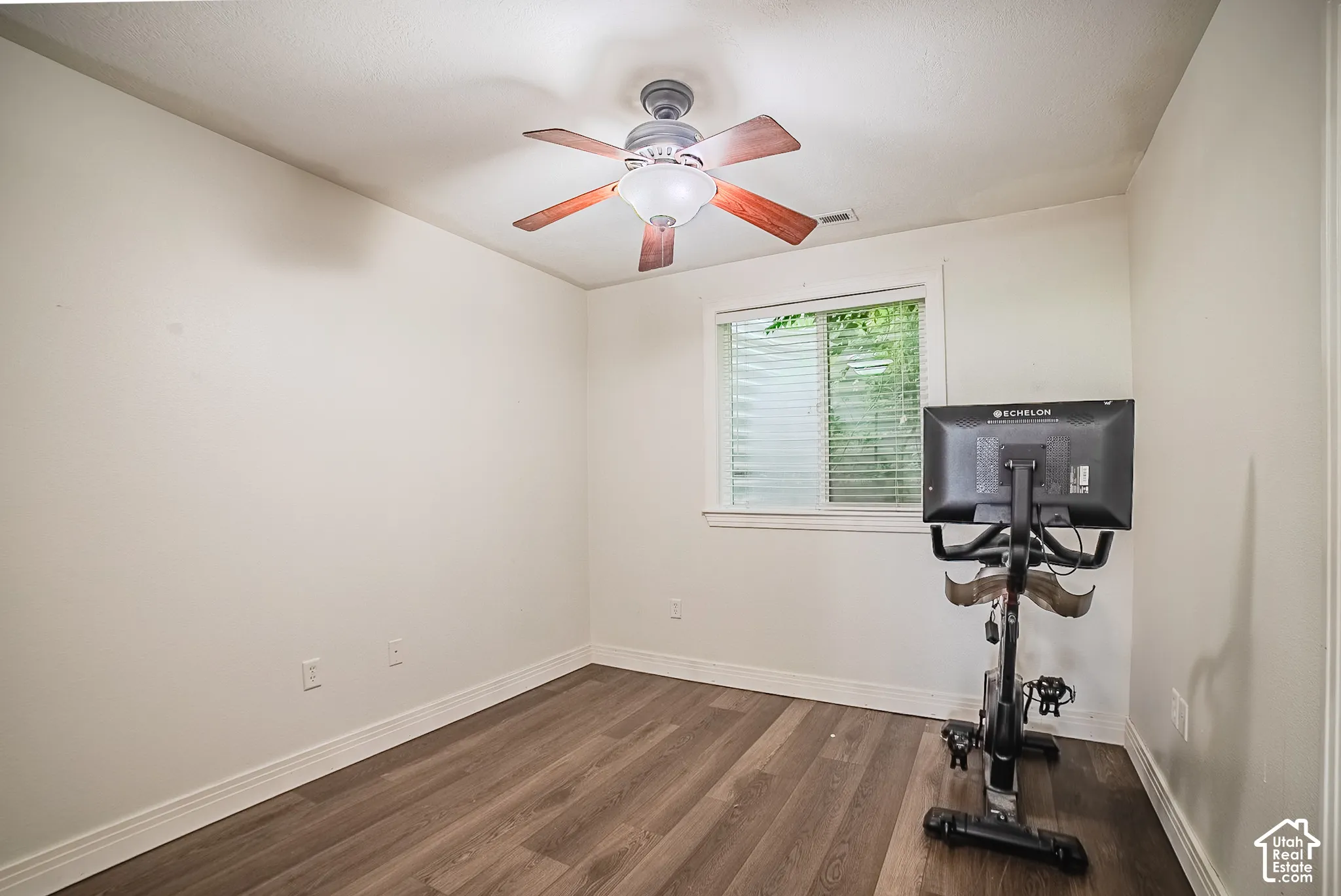 Wood-finish flooring with a ceiling fan light fixture and a window with horizontal blinds