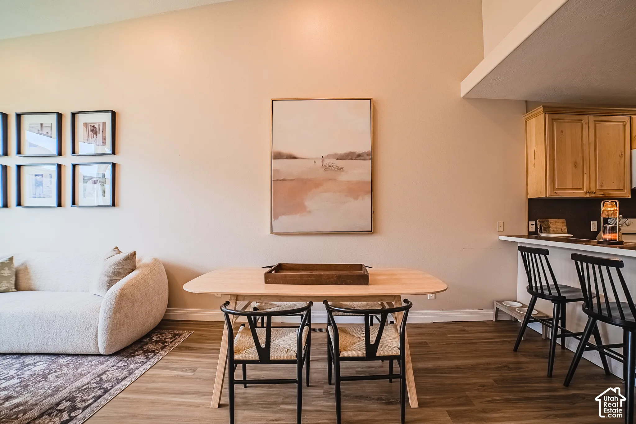 Vaulted ceilings, wood-finish flooring, light wood cabinetry, and a kitchen peninsula with bar seating