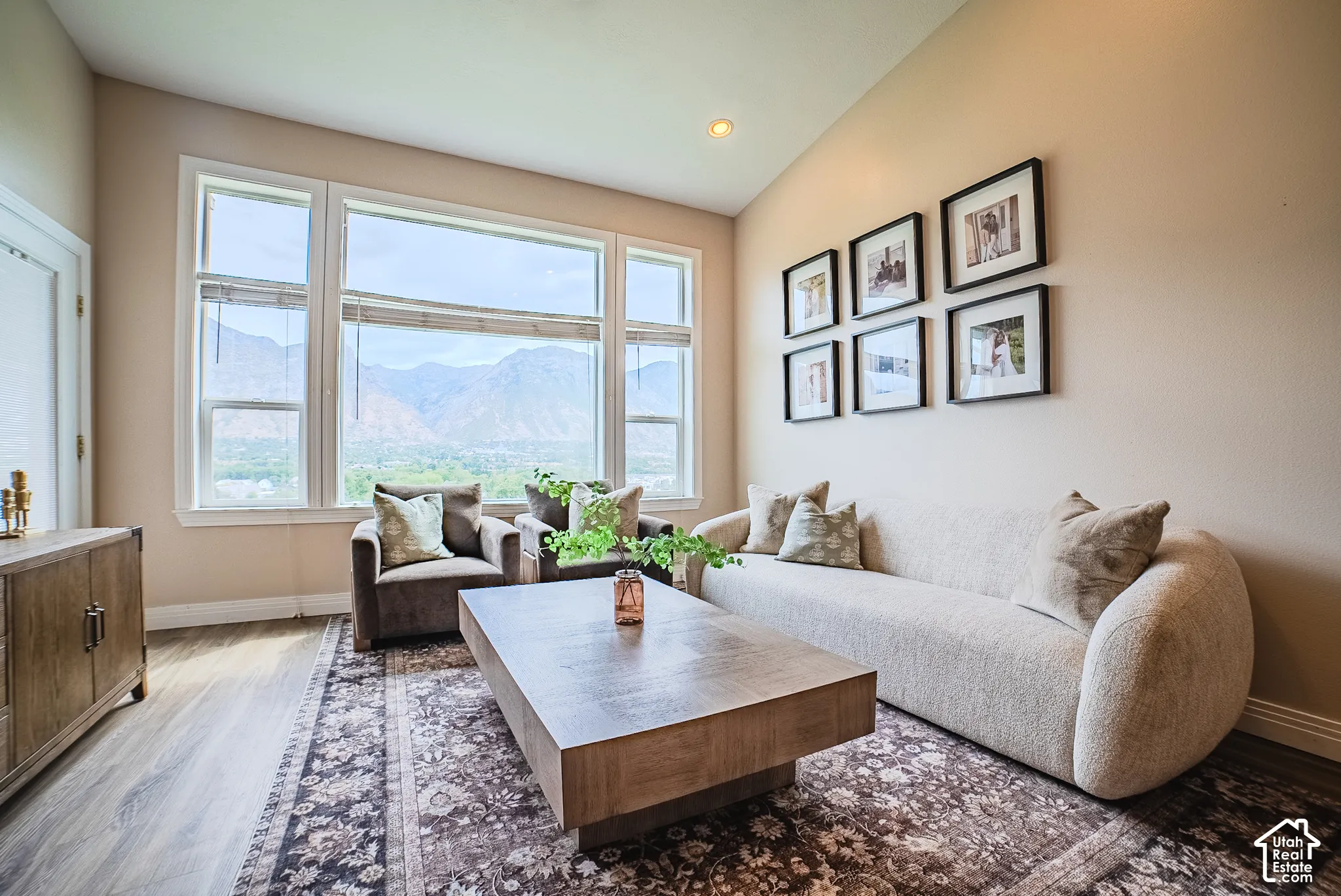 Expansive window wall with mountain scenery, vaulted ceiling with recessed lighting, and wood-finish flooring