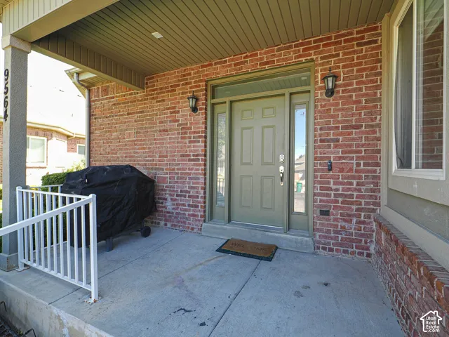 Welcoming covered entry featuring a brick exterior, solid wood-panel entry door with sidelights, recessed lighting, and a concrete porch with white metal railing