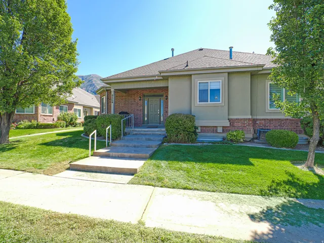 Brick and stucco exterior with a covered porch, concrete entry steps, and mature landscaping