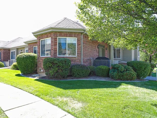 Brick exterior with multiple windows, a covered patio, and mature landscaping