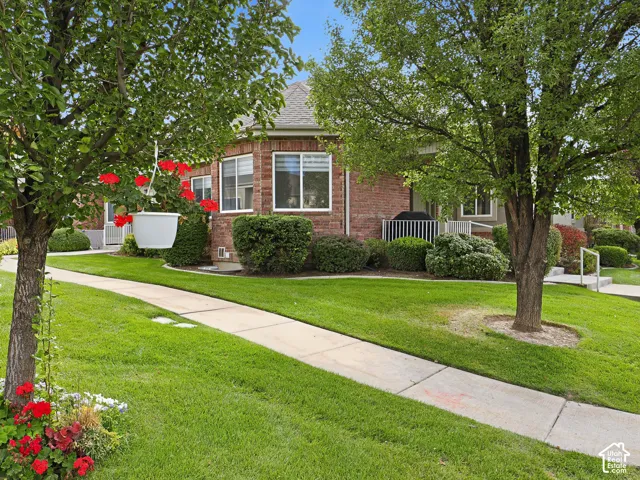 Brick exterior with a faceted bay window, concrete walkways, mature deciduous trees, and manicured shrubbery