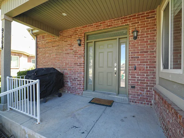 Welcoming covered entry featuring a brick exterior, solid wood-panel entry door with sidelights, recessed lighting, and a concrete porch with white metal railing