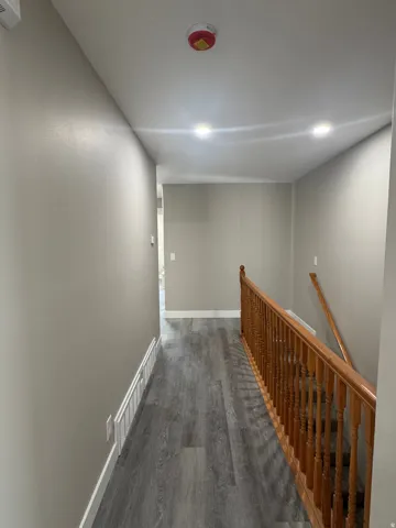 Wood-finish flooring, staircase with wood railing, recessed ceiling lighting, and neutral wall paint