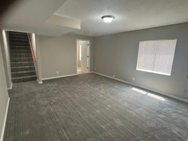 Spacious room featuring neutral wall paint, gray carpet flooring, a window with blinds, and an overhead flush-mount light fixture