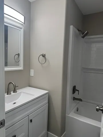 Main Floor Bathroom featuring a white vanity with an integrated sink, brushed nickel faucet, framed mirror, and a shower-over-tub combination with subway tile surround