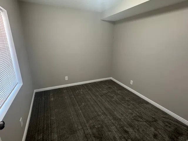Neutral wall paint, textured carpet flooring, white trim, and a window with blinds