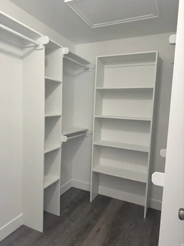 Primary Closet White built-in shelving, white hanging rods, and wood-finish flooring