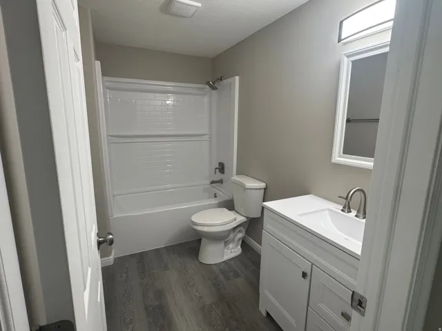 Bathroom featuring wood-finish flooring, a white vanity with integrated sink, a framed mirror, and a white subway tile-style bathtub surround