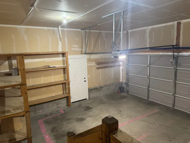 Attached garage featuring concrete flooring, overhead lighting, a panel garage door, and a permanent wooden shelving unit