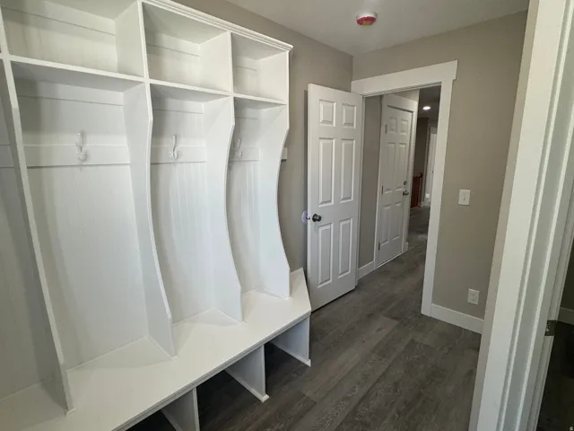 Dedicated mudroom featuring three built-in cubbies with upper shelving, individual bench seating with storage beneath, and wood-finish flooring
