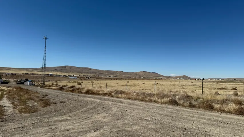 Gravel drive leading to a property featuring a wind turbine and a distant mountain range