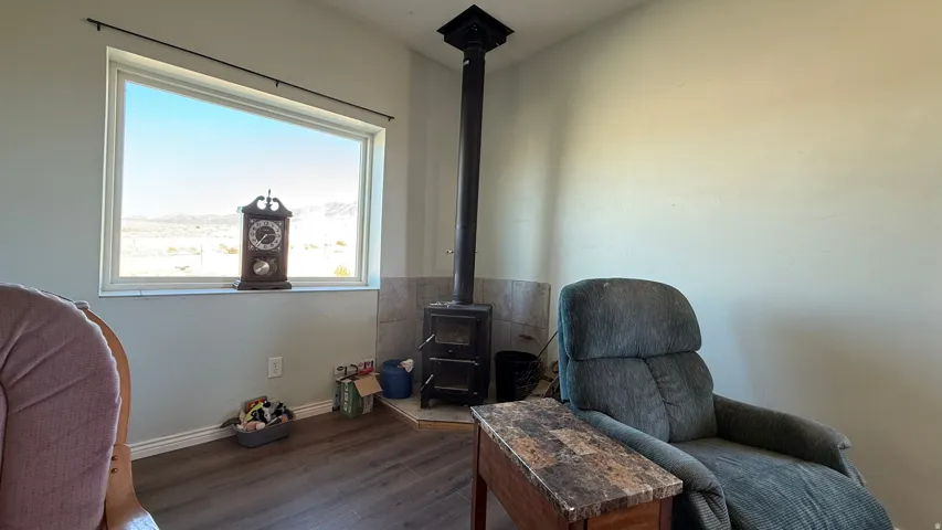 Wood-finish flooring, a large horizontal window, a corner wood-burning stove with a tile surround, and light-toned walls