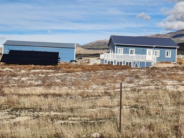 Blue exterior siding, white trim, metal roofing, white deck with railings, and a detached outbuilding with solar panels