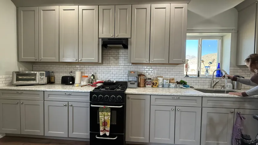 Gray shaker-style cabinetry with chrome hardware, white subway tile backsplash, light-toned countertops, and a stainless steel sink with a gooseneck faucet