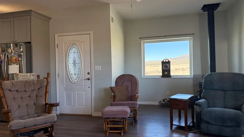 Wood-finish flooring, white paneled door with decorative glass insert, gray cabinetry, stainless steel refrigerator, and a wood-burning stove with a black flue