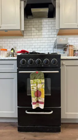 Black range with four burners, subway tile backsplash, light-toned upper and lower cabinetry, and wood-finish flooring