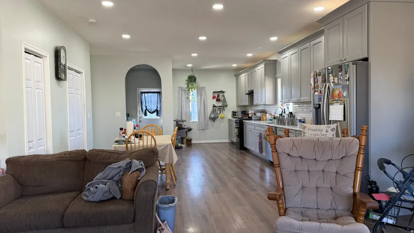 Open-concept living area with recessed lighting, wood-finish flooring, and a kitchen featuring gray shaker-style cabinetry, stainless steel appliances, and a tile backsplash