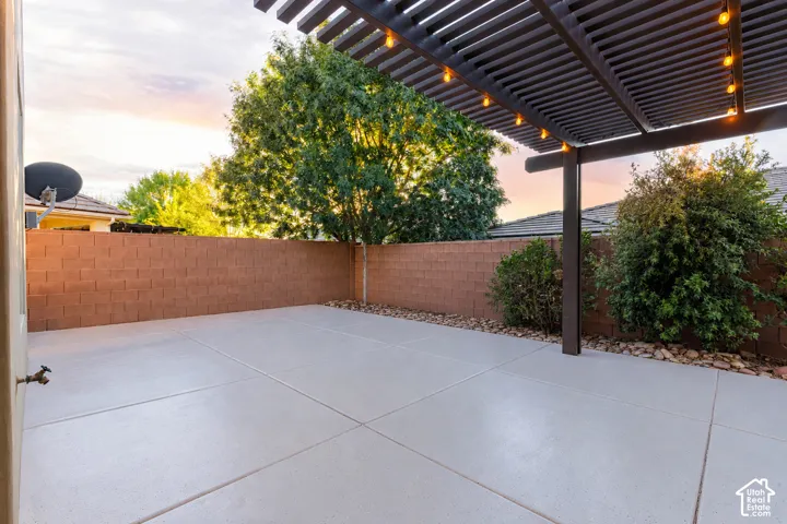 Patio: Extended concrete patio under the string-lit pergola, framed by the block wall