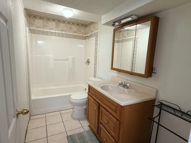Bathroom with a tub/shower combination, decorative tile surround, wood-finish vanity with an integrated sink, and a mirrored medicine cabinet