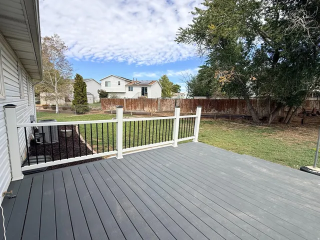 Spacious composite deck with white railings and black balusters, overlooking a fenced backyard with mature trees