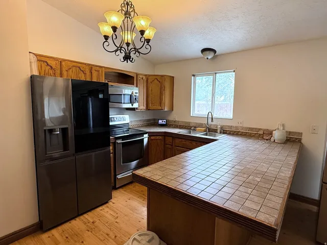 Kitchen featuring wood cabinetry, tile countertops, stainless steel appliances, wood-finish flooring, and a window