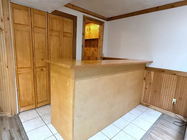 Wood-finish bar with a glossy countertop, white tile flooring, wood-finish paneling, and folding closet doors