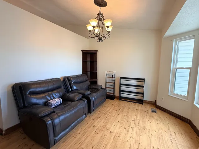Vaulted ceiling with an ornamental chandelier, wood-finish flooring, and a bay window