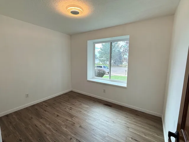 Wood-finish flooring with white trim and a single window offering natural light