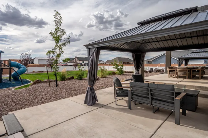 Paved patio area, metal-roofed gazebo, gravel landscaping, manicured lawn, and privacy fencing