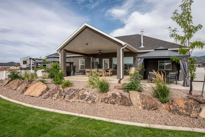 Modern home featuring a covered patio with ceiling fans, expansive grounds with native landscaping and natural stone accents, manicured lawn, and a detached structure