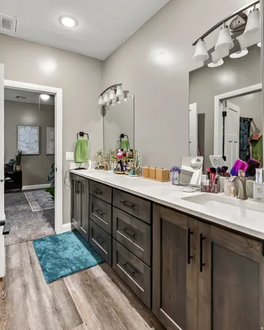 Dual vanity with integrated sinks, dark wood-finish cabinetry, light stone-finish countertops, and wood-finish flooring