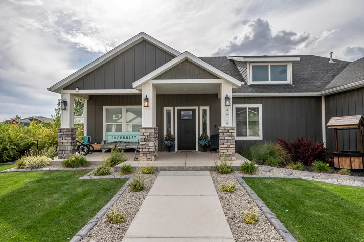 Dark gray exterior siding with white trim, stone-clad porch columns, a dark entry door with sidelights, and a dormer window
