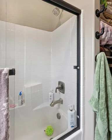 Tub/shower combination featuring a showerhead, brushed nickel fixtures, and a glass shower enclosure with a dark frame