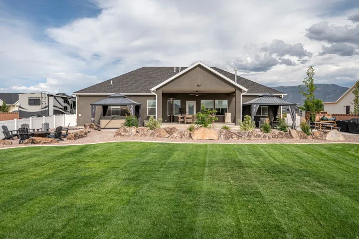 Expansive green lawn, stucco exterior, covered patio, gravel landscaping with large rocks, two permanent gazebos