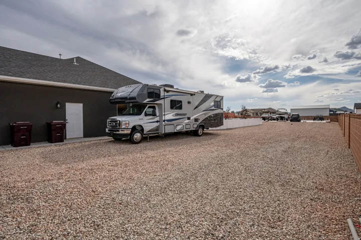 Extended gravel driveway with ample parking space, a white privacy fence, and a block wall perimeter
