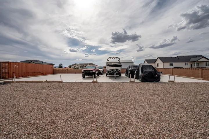 Expansive gravel lot with a large concrete pad, enclosed by a block wall and a shipping container