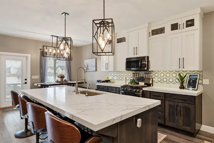 Kitchen featuring a large island with a waterfall countertop, hexagon tile backsplash, two-tone cabinetry, and wood-finish flooring