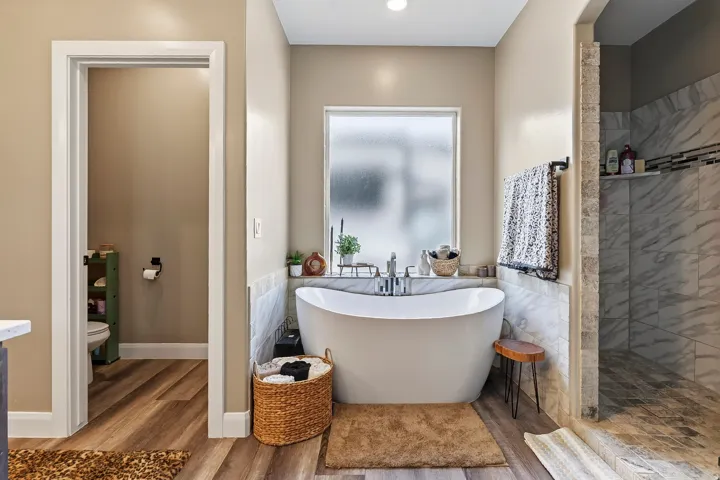 Freestanding soaking tub with chrome fixtures, wood-finish flooring, and a tiled shower with a built-in shelf