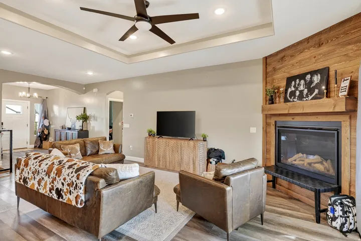 Recessed lighting, ceiling fan, tray ceiling, wood-look flooring, and a fireplace with a wood-plank accent wall
