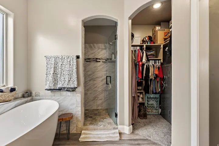 Freestanding soaking tub, walk-in shower with glass enclosure, marble-style tile, recessed lighting, and an arched entry