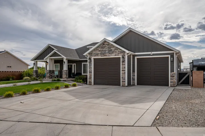 Exterior featuring stacked stone accents, dark-toned siding, a covered front porch, and a concrete driveway leading to a two-car garage