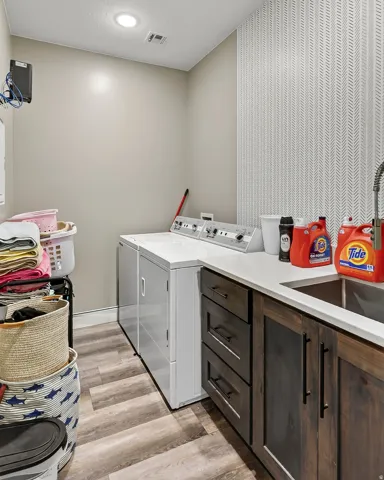 Wood-finish flooring, dark wood cabinetry with matte black hardware, white countertop, stainless steel sink with a gooseneck faucet, and recessed lighting