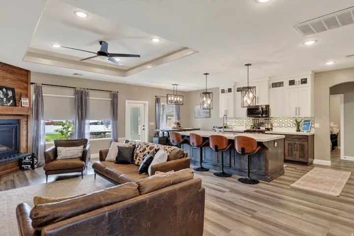 Open-concept living space featuring wood-finish flooring, a tray ceiling with recessed lighting, and a modern ceiling fan