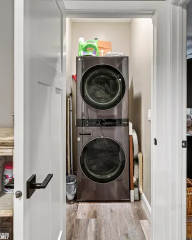Dedicated laundry closet with stacked appliances and wood-finish flooring