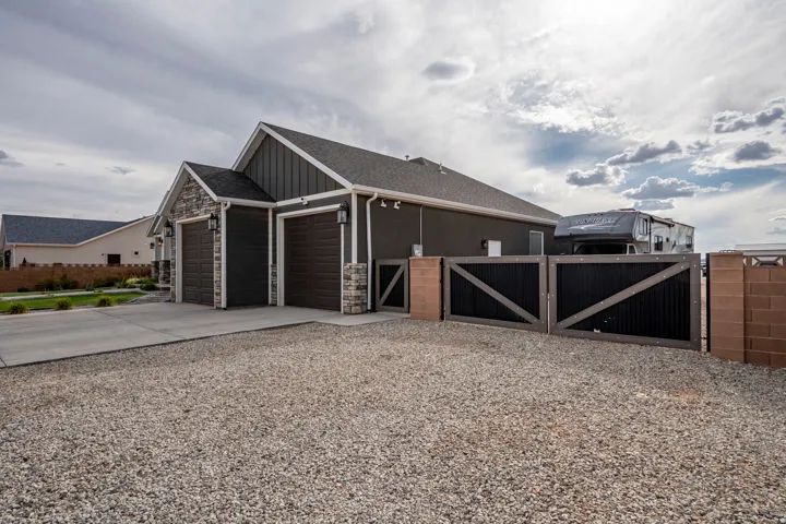 Gable roofline with stone accents, board and batten siding, two-car garage, concrete driveway, and gravel parking area