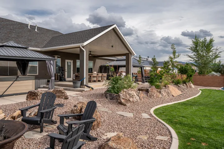 Expansive yard featuring a manicured lawn, a rock garden with mature plantings, and a covered patio