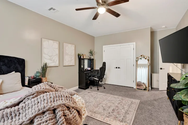Spacious primary bedroom suite with dual closets, ceiling fan with integrated lighting, and dedicated work-from-home office space featuring built-in desk and shelving
