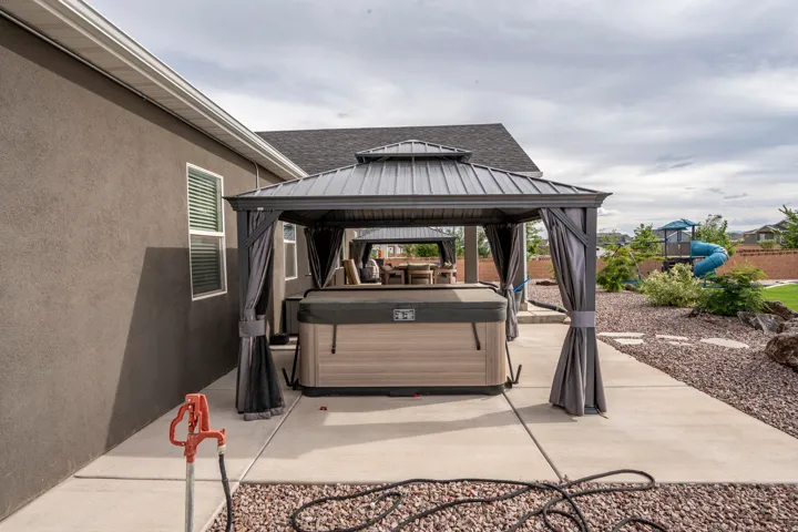 Patio with covered gazebo featuring a hot tub, concrete paving, and surrounding gravel landscaping